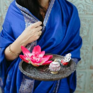 A woman in traditional attire holding a lotus flower on a tray, symbolizing beauty and grace.