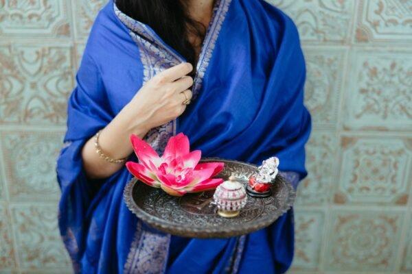 A woman in traditional attire holding a lotus flower on a tray, symbolizing beauty and grace.